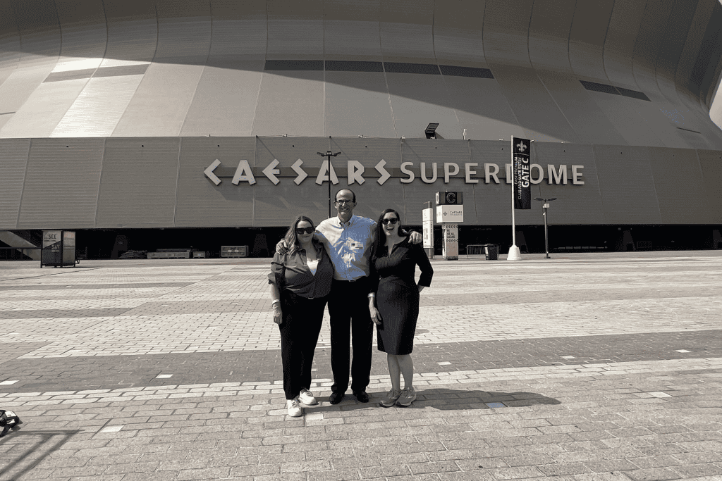 Group of three people posing in front of the Caesars Superdome, showcasing the iconic venue's distinctive architecture and branding.