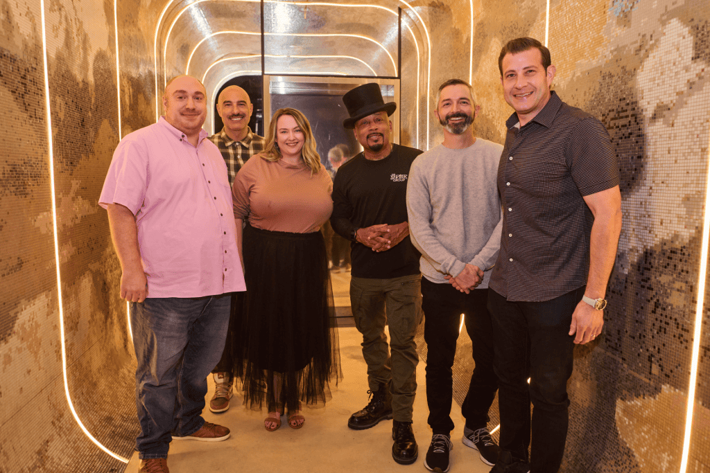 Group of five individuals posing together in a stylish, illuminated hallway, emphasizing teamwork and collaboration in marketing strategies.