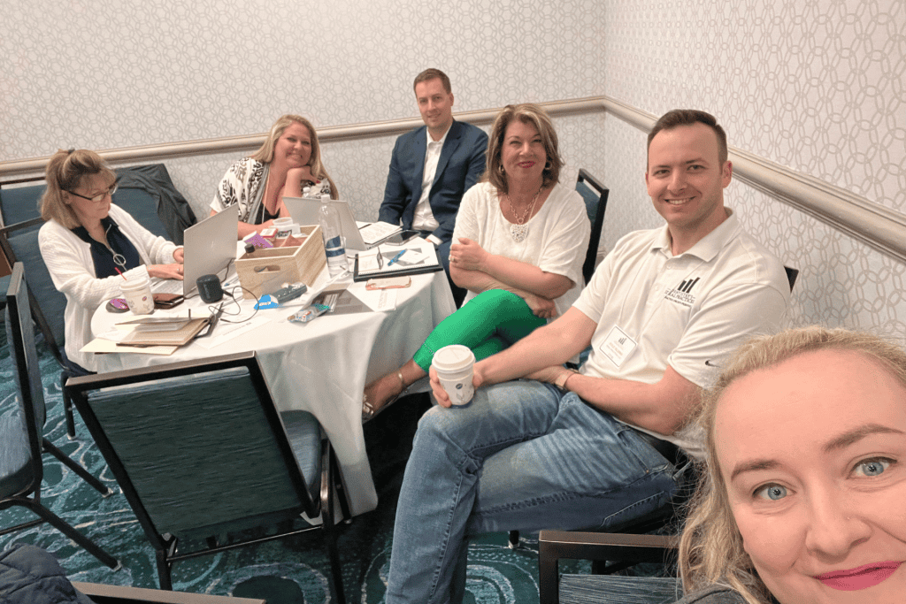Group of marketing professionals collaborating at a round table, discussing strategies while using laptops and notes, emphasizing teamwork in PPC advertising and online business growth.