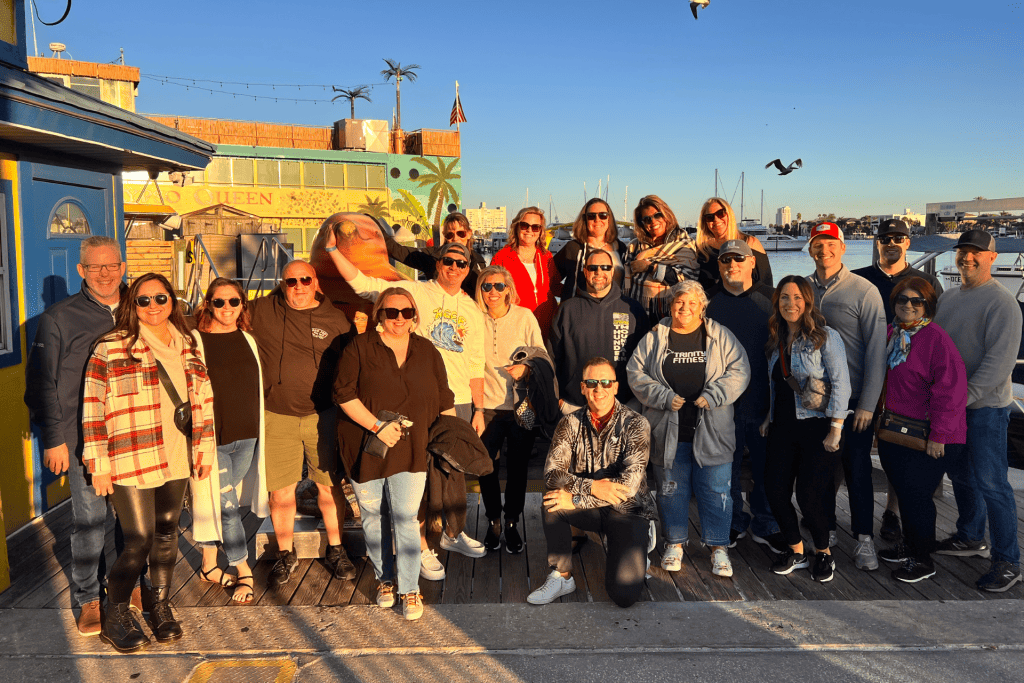 Group of people posing together at a waterfront location, with a colorful building in the background, symbolizing community and collaboration in marketing strategies.